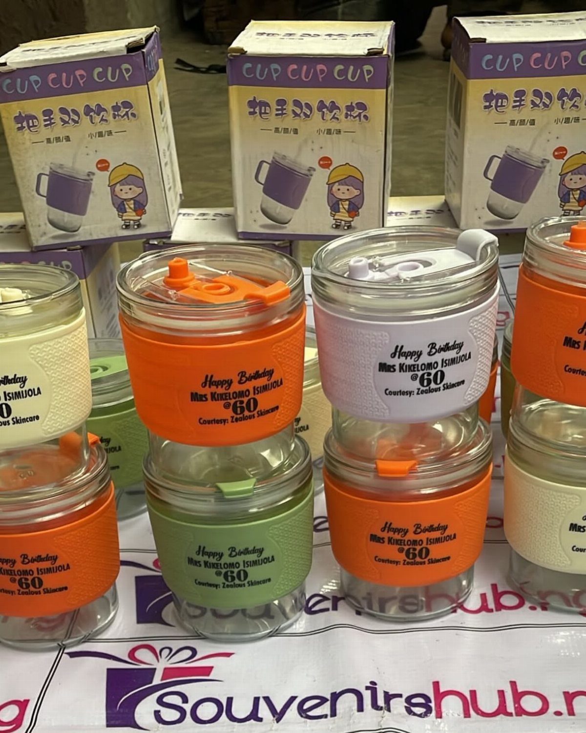 Colorful glass mugs with personalized birthday text on silicone sleeves arranged on a table.