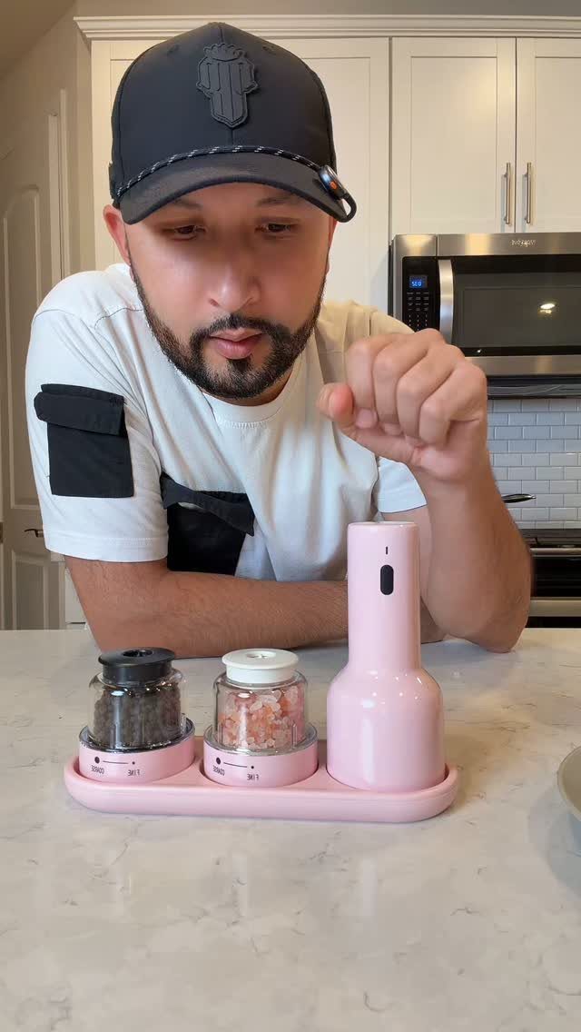 A man using a pink electric salt and pepper grinder set on a kitchen counter.