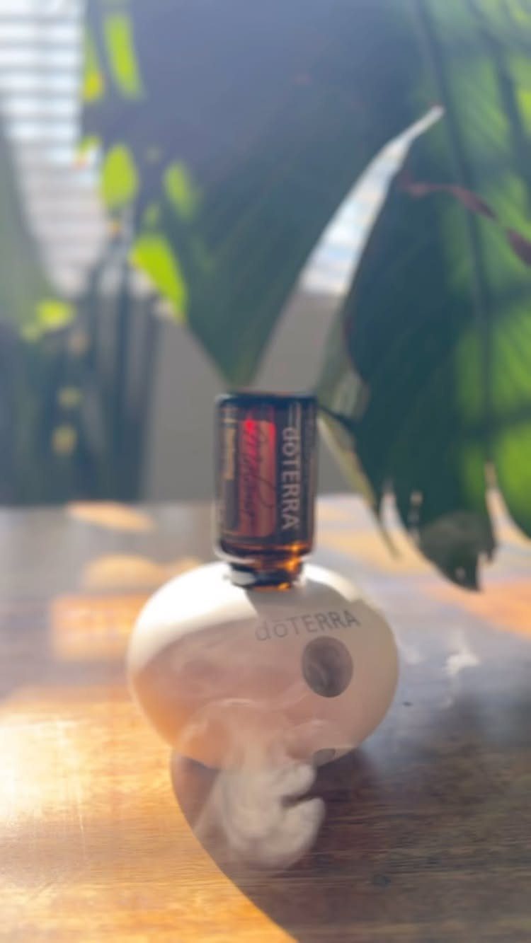 A white egg-shaped essential oil diffuser emitting mist with an amber oil bottle on top.