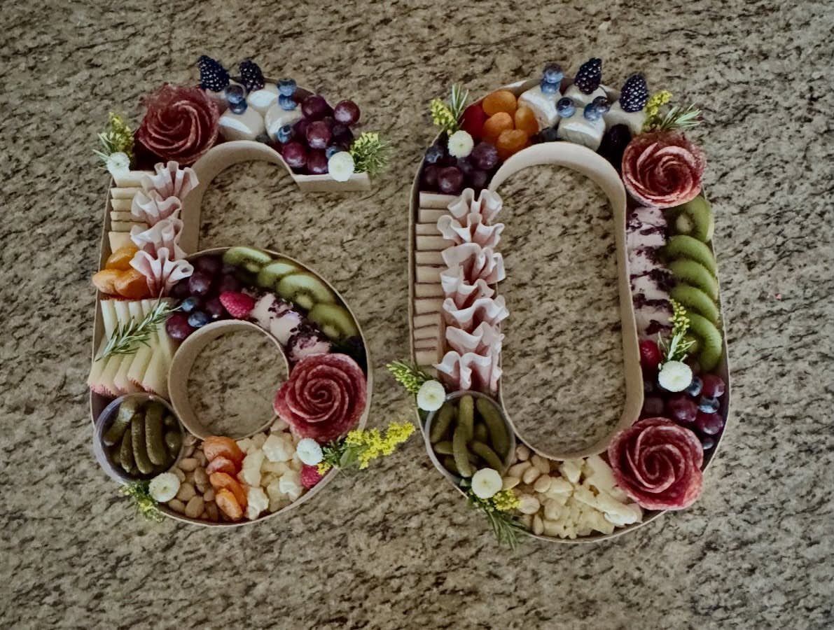 Charcuterie spread arranged in the shape of the number sixty with meats, cheeses, and fruits.