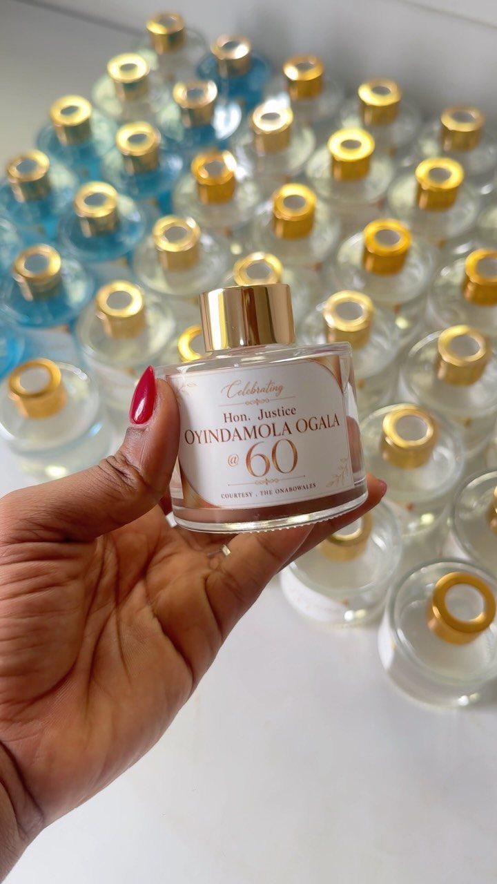 A hand holding a personalized perfume bottle celebrating a 60th birthday with many bottles in the background.