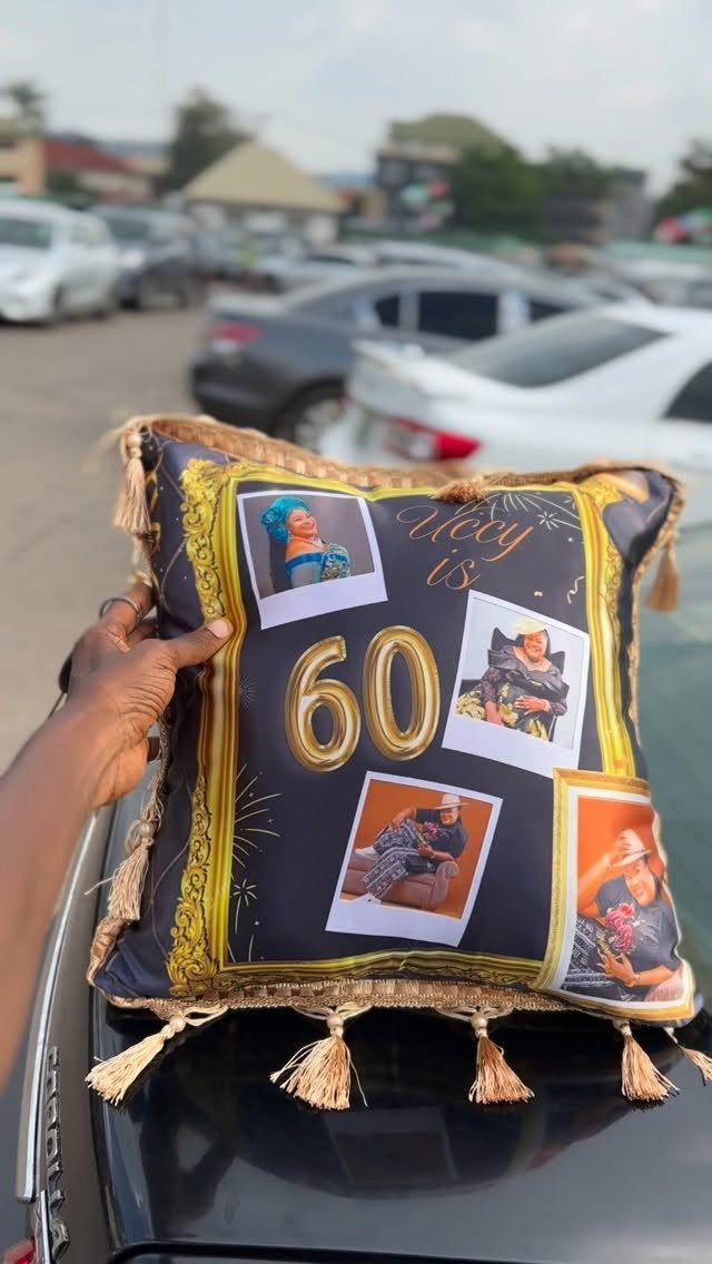 A hand holding a personalized black pillow decorated with photos and the number 60.