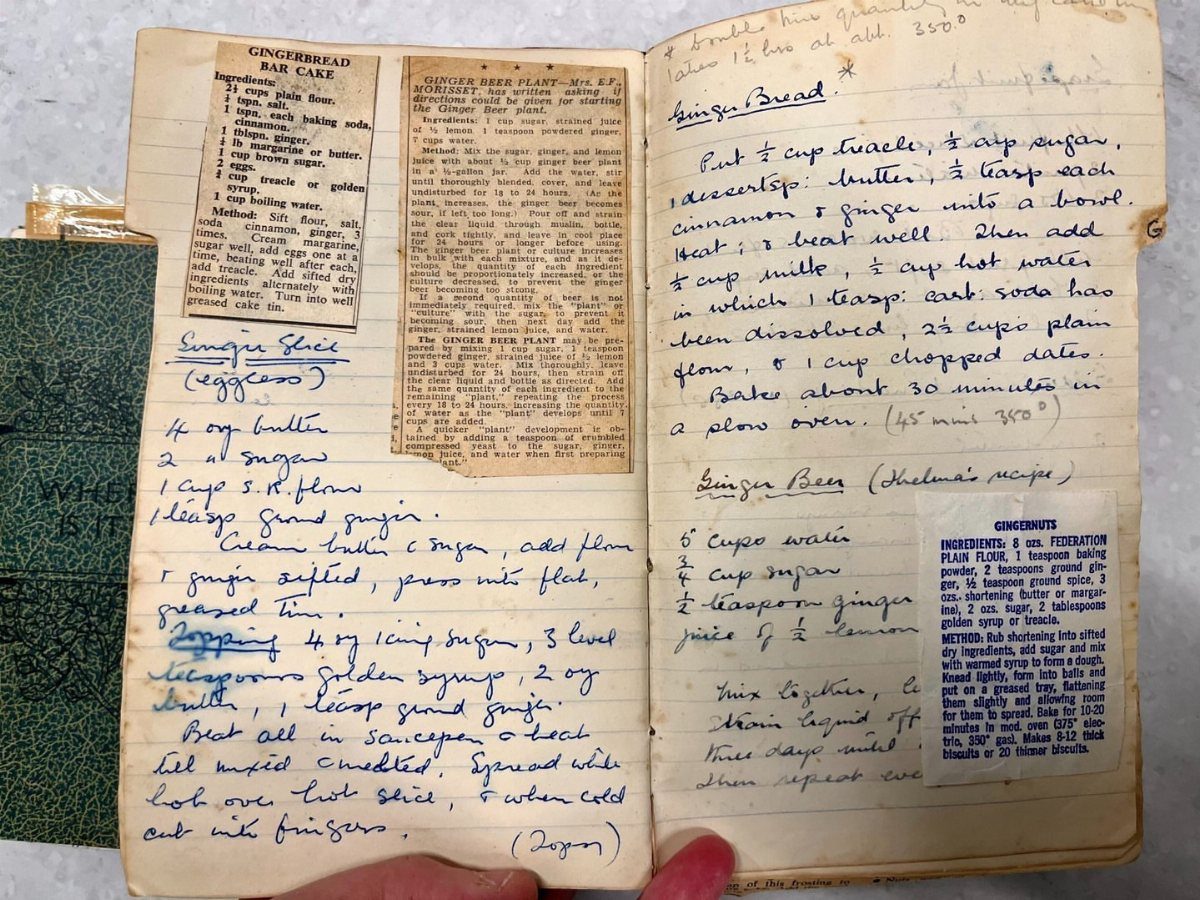 An open vintage notebook containing handwritten and printed recipes on aged paper.