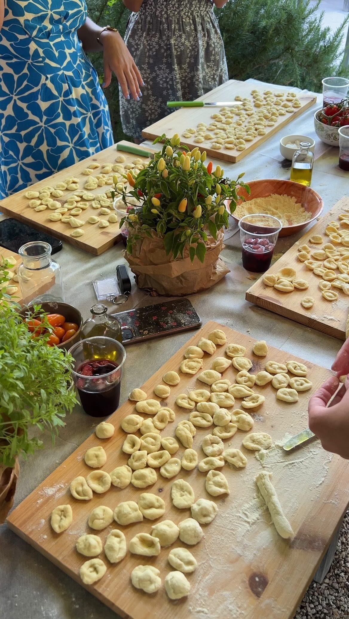 People preparing small pieces of dough on wooden boards during an outdoor cooking activity.