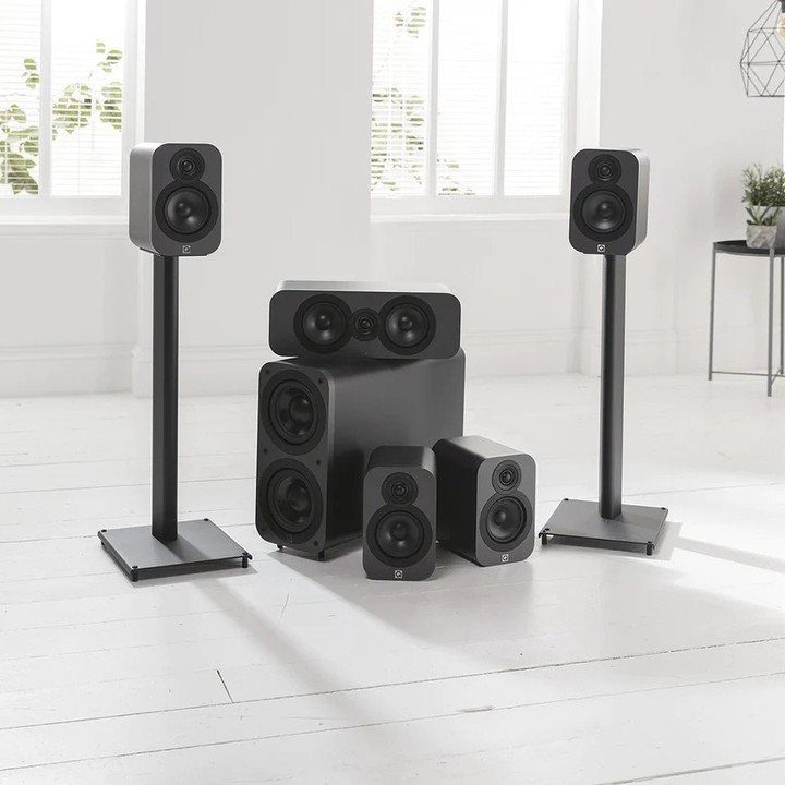 Black high-fidelity home theater speaker system arranged on a white wooden floor.