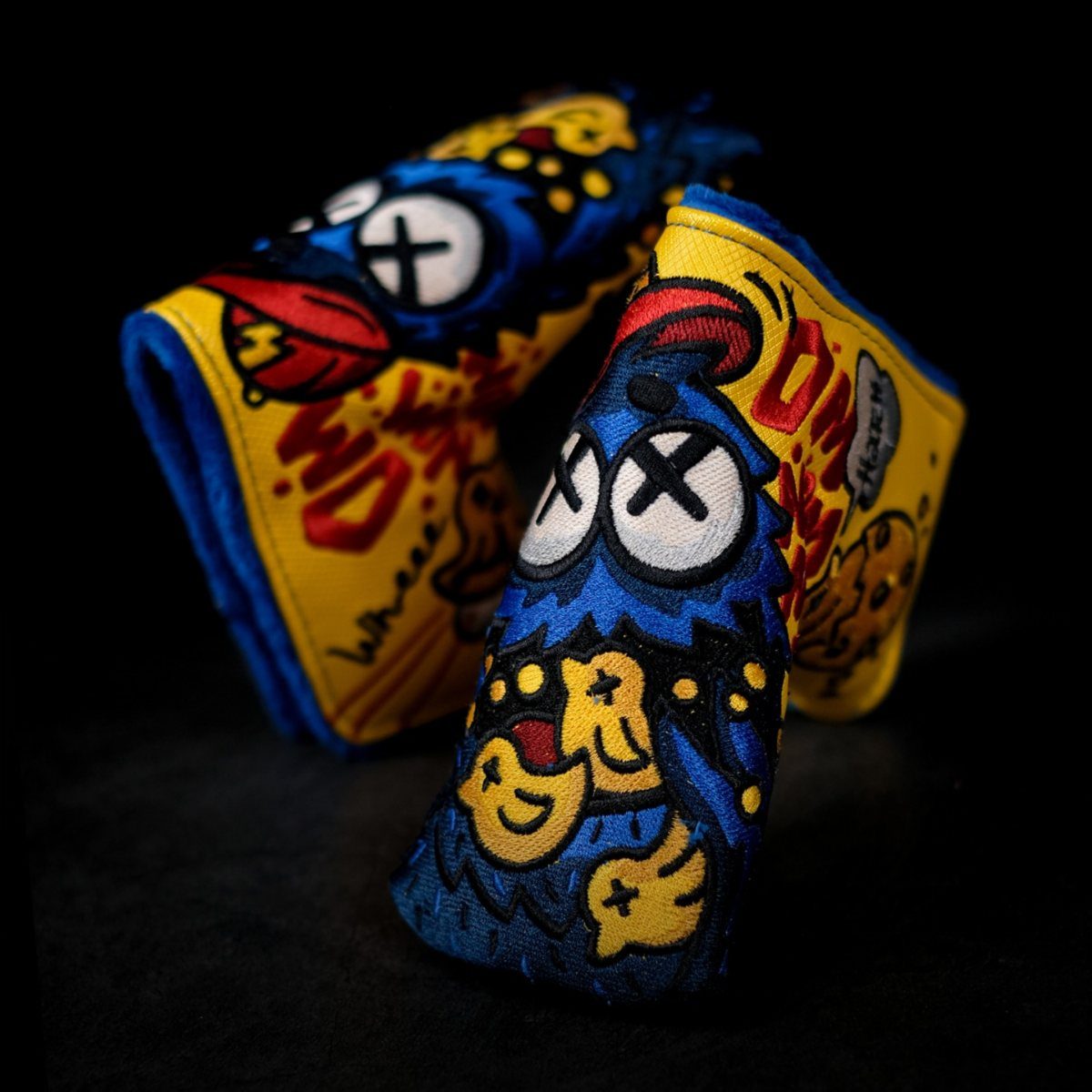 Two vibrant, cartoon-style embroidered golf club headcovers resting on a black surface.