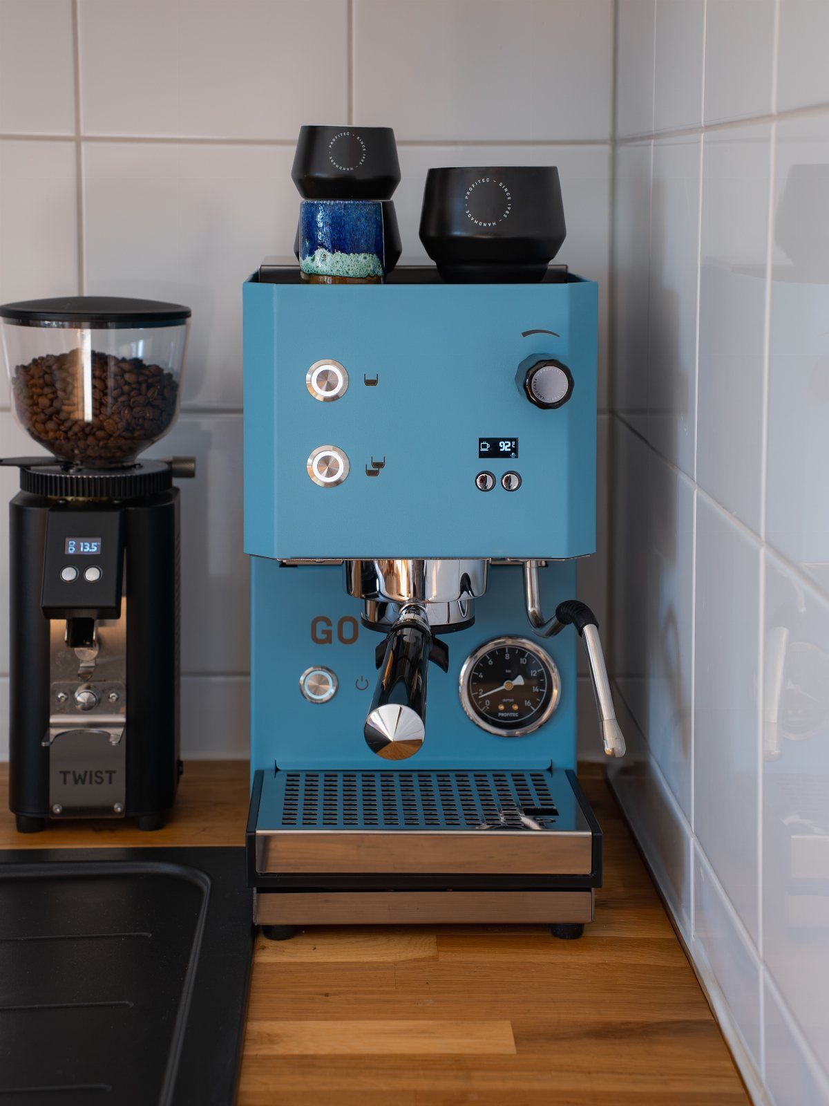 A bright blue retro espresso machine and a black coffee grinder on a wooden counter.
