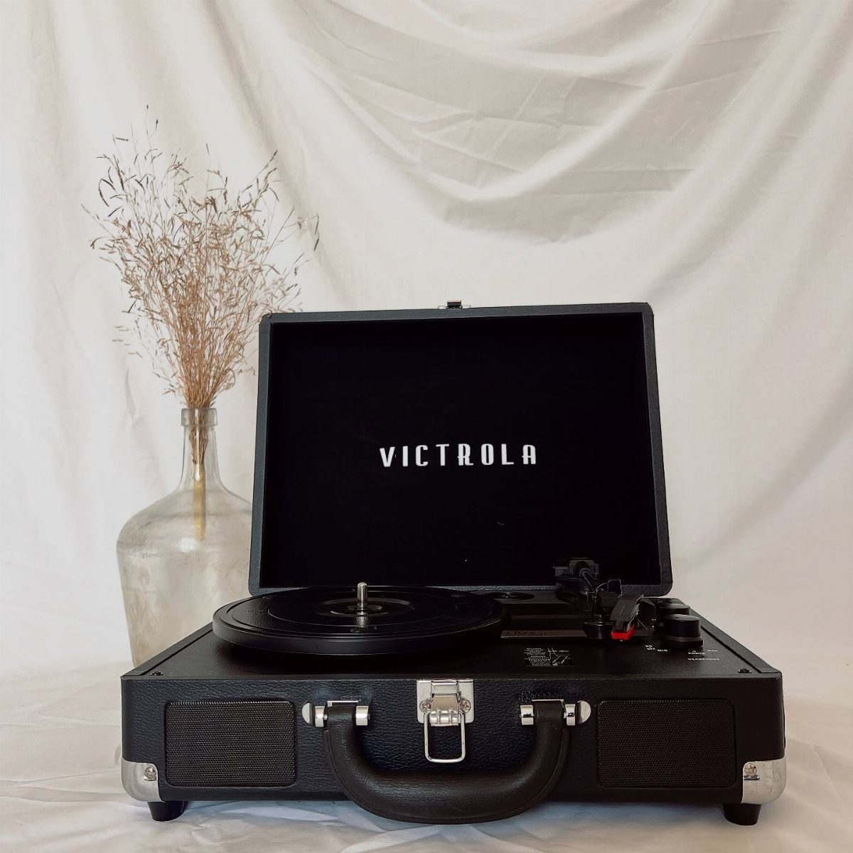A black Victrola suitcase record player with a vinyl record on a white background.