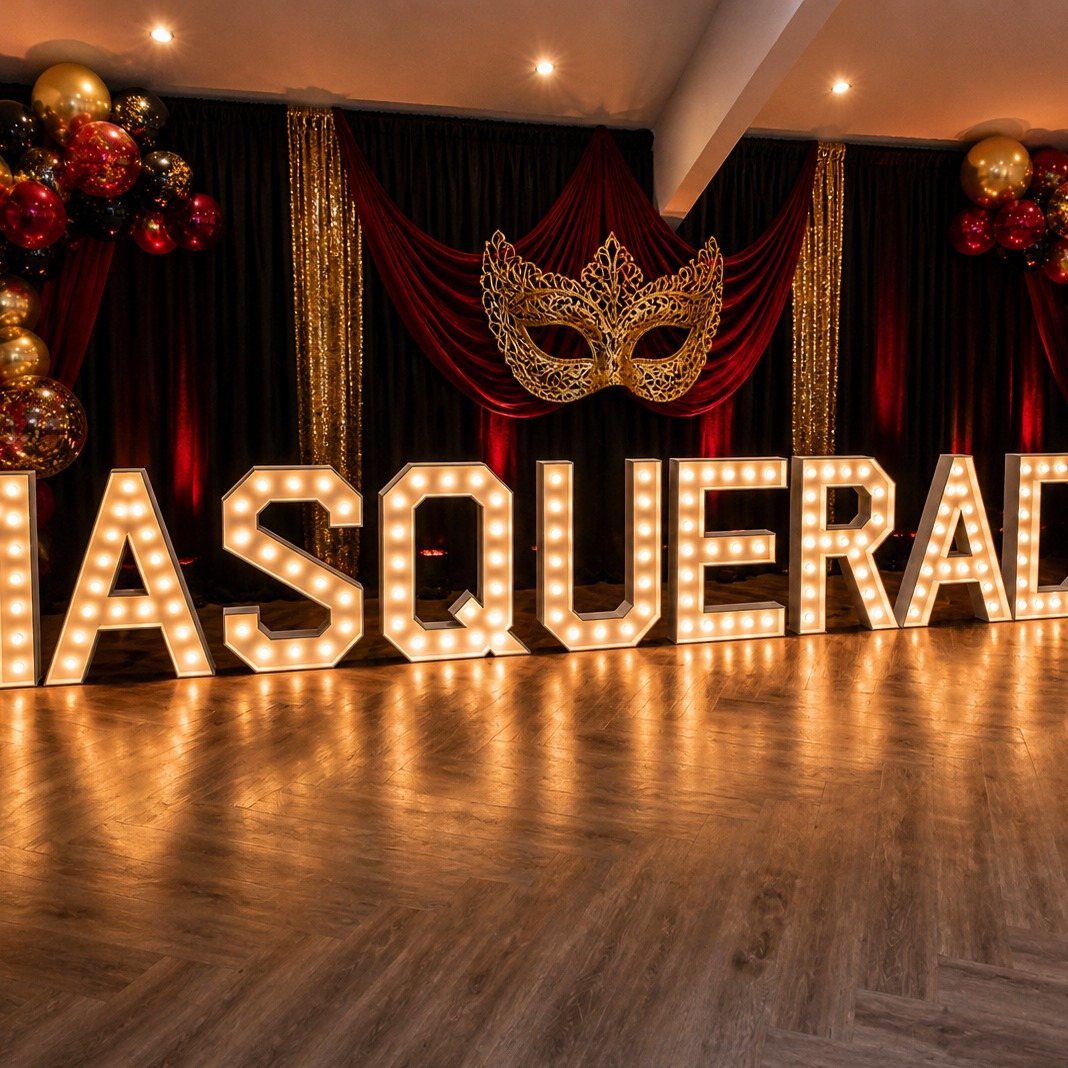 Large illuminated marquee letters spelling MASQUERADE on a wooden floor with festive decorations.