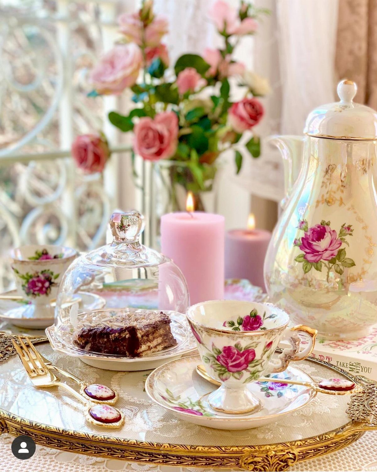 Elegant tea set with floral teacups, cake, and pink roses on a gold tray.