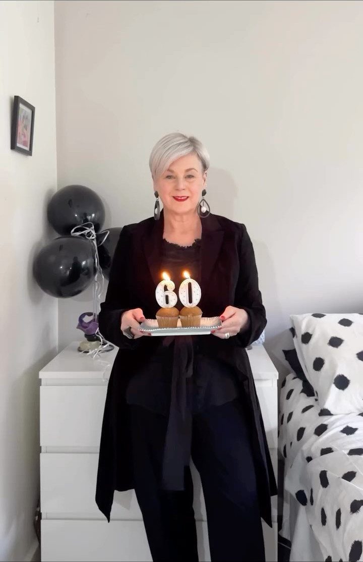 A woman in a black outfit holding cupcakes with lit number 60 candles.
