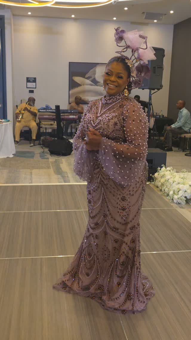 A smiling woman wearing a beaded mauve formal gown and a large floral headpiece.