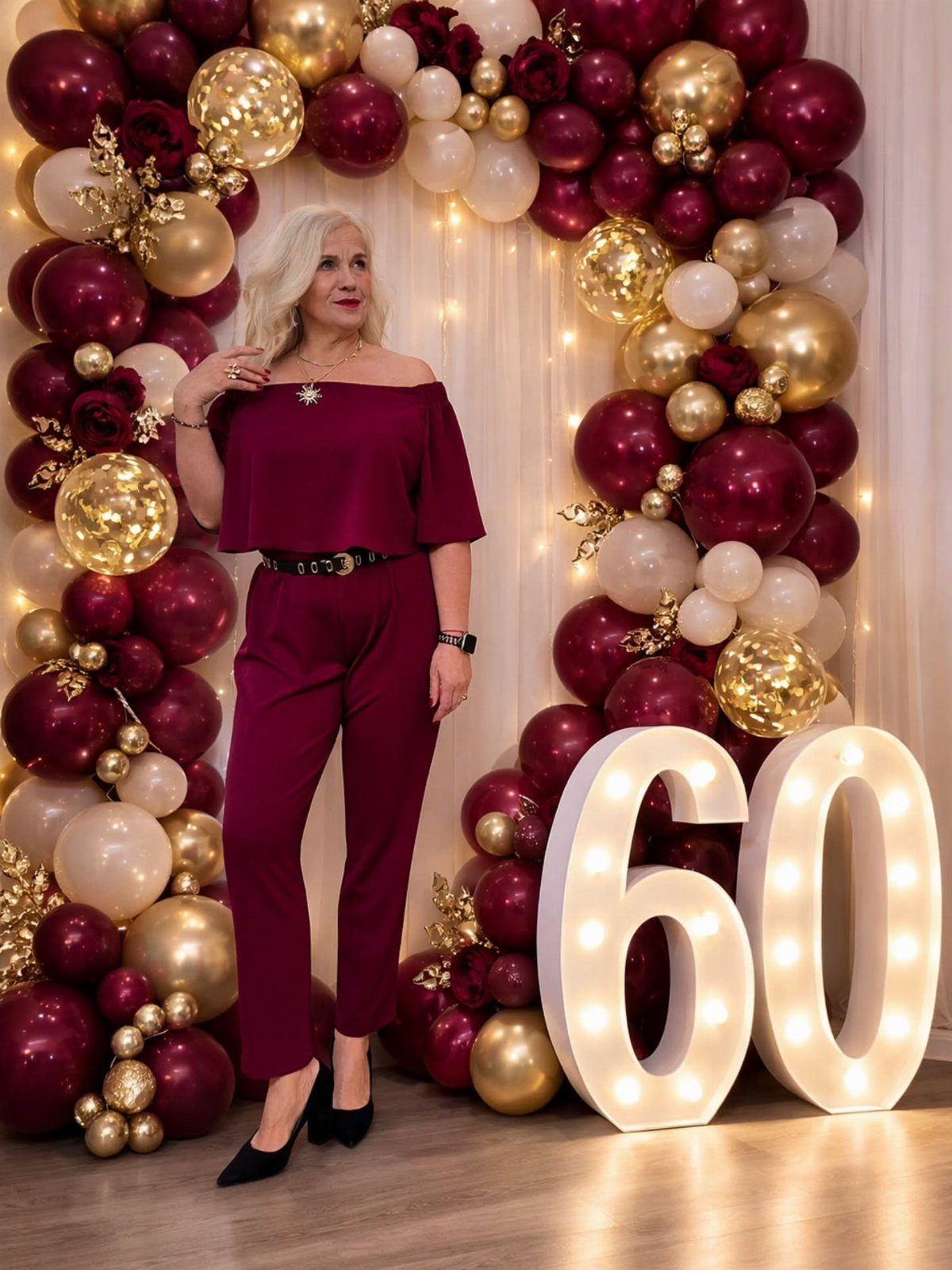 Woman in a maroon off-the-shoulder blouse and trousers standing by large illuminated numbers.