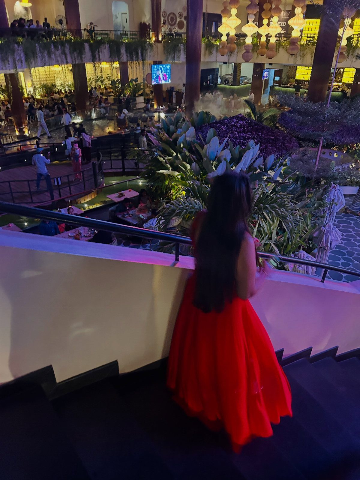 A person in a long red maxi dress standing on a staircase in a large atrium.