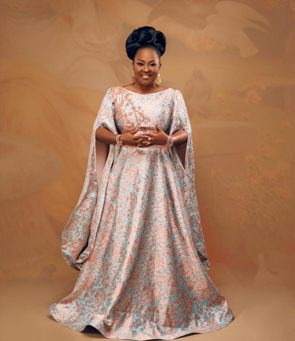 Smiling woman wearing a long-sleeved, light blue and gold patterned damask gown.