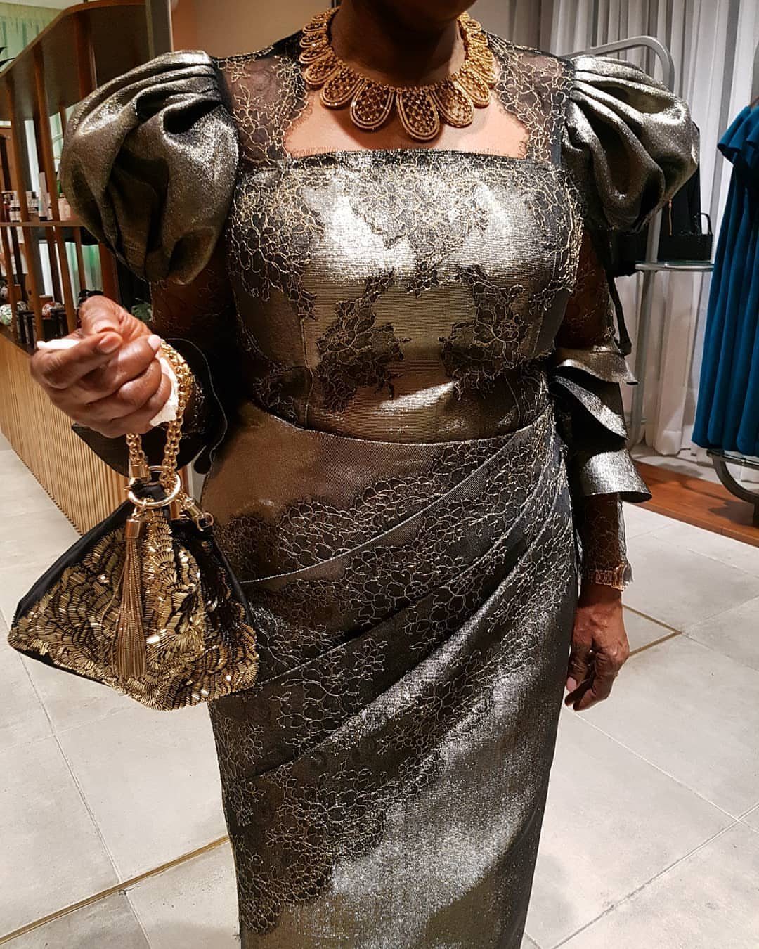 Person wearing a metallic gold lace dress with puffed sleeves and gold jewelry.