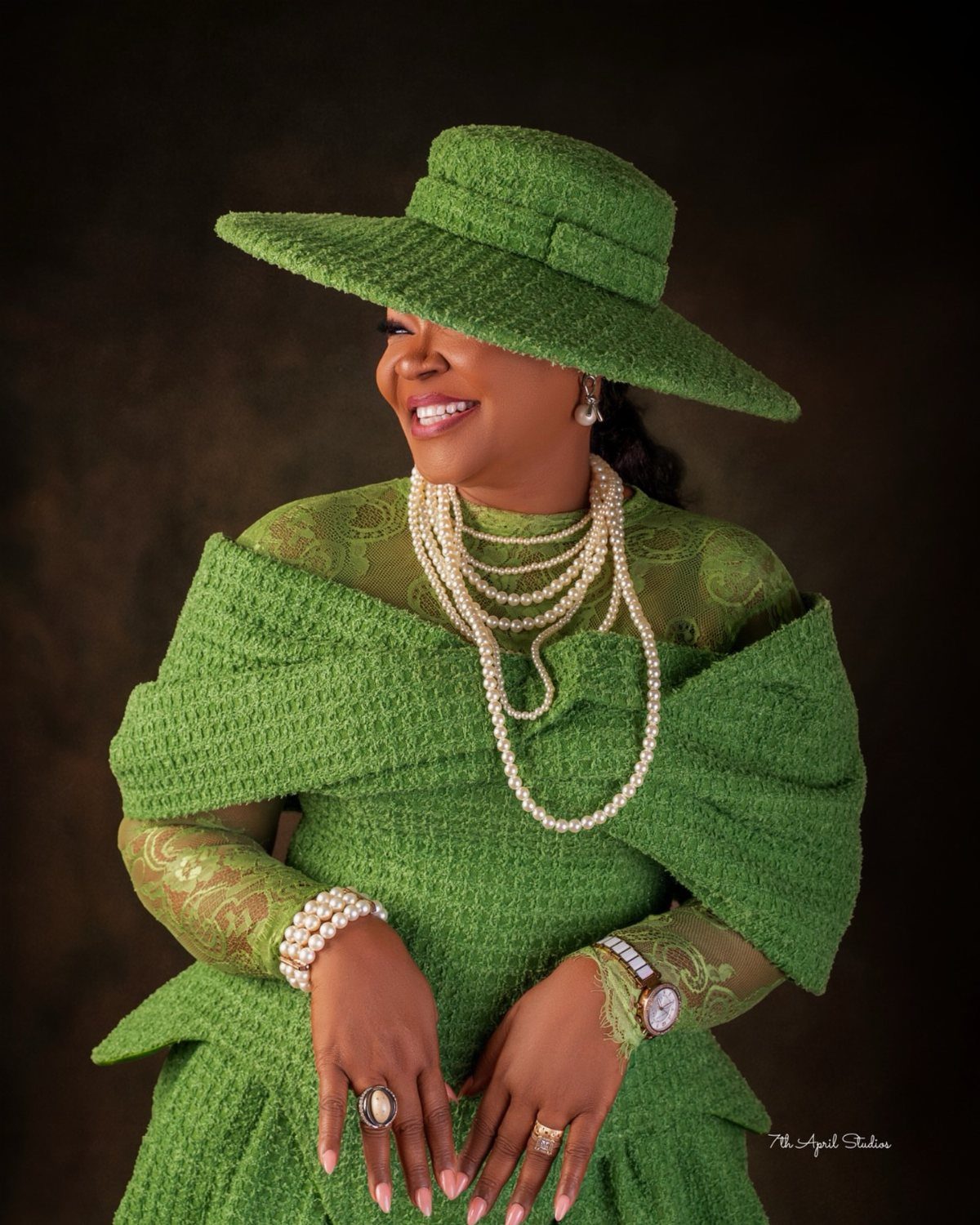 A smiling woman wearing a bright green textured cocktail dress and matching wide-brimmed hat.