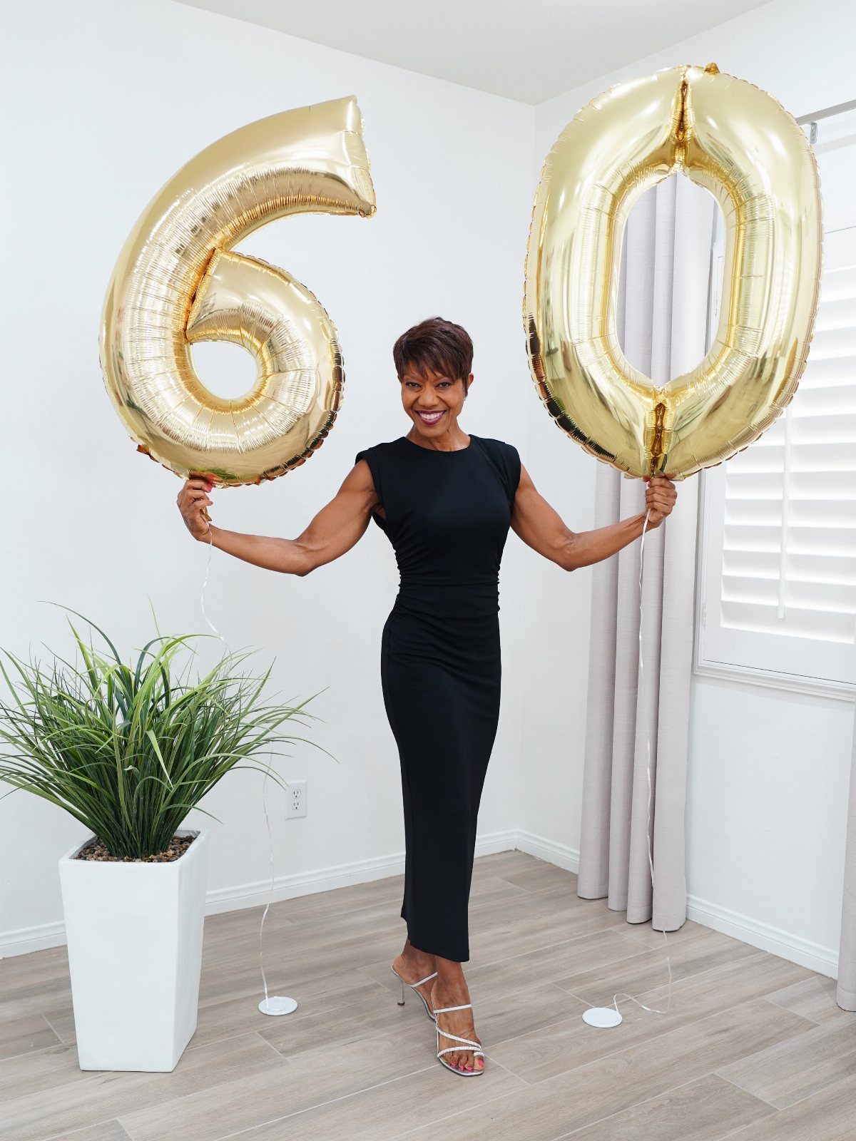 A woman in a black midi dress holding large gold number sixty balloons.