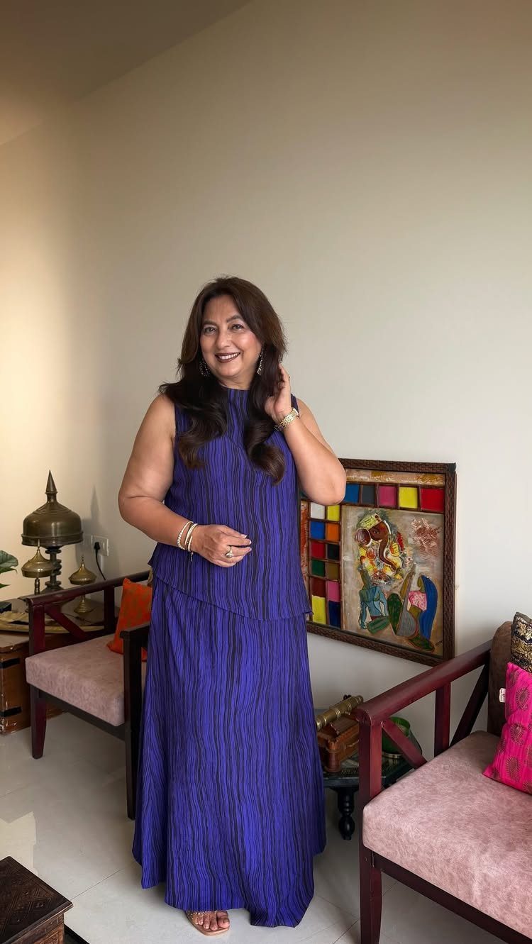A woman in a long, sleeveless pleated royal blue dress smiling in a living room.