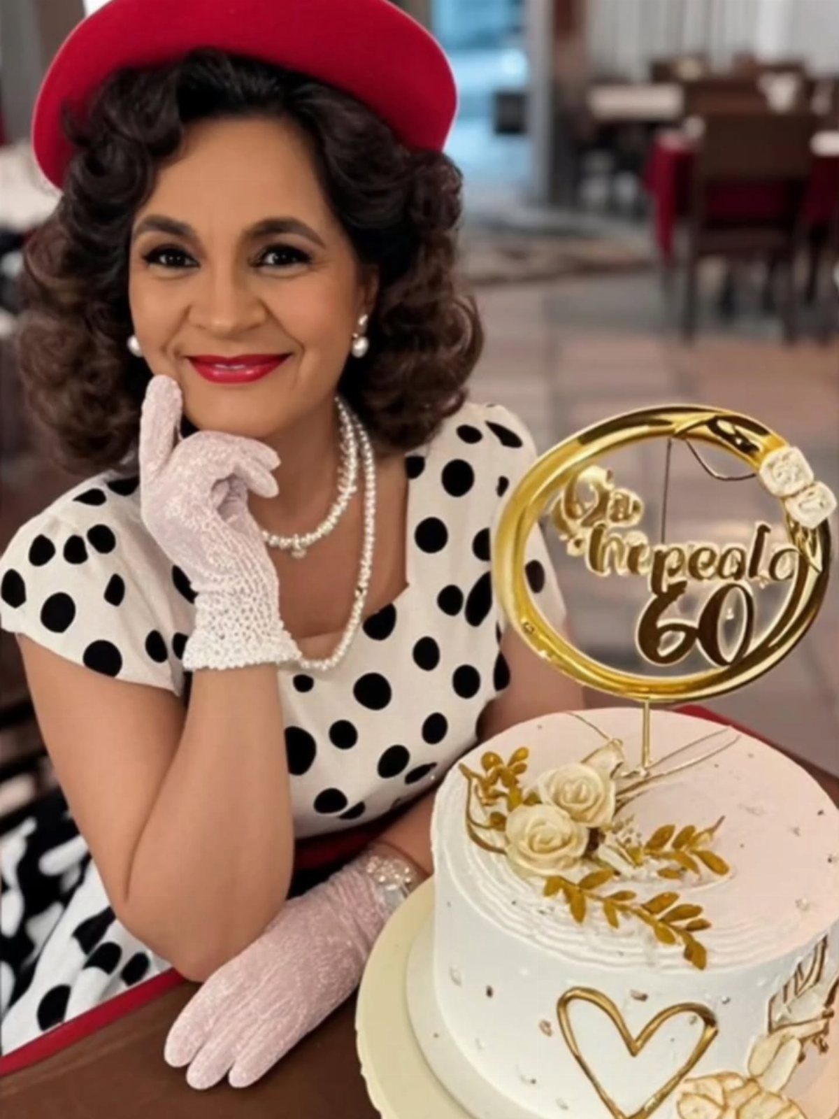 A woman in a black and white polka dot dress posing next to a birthday cake.