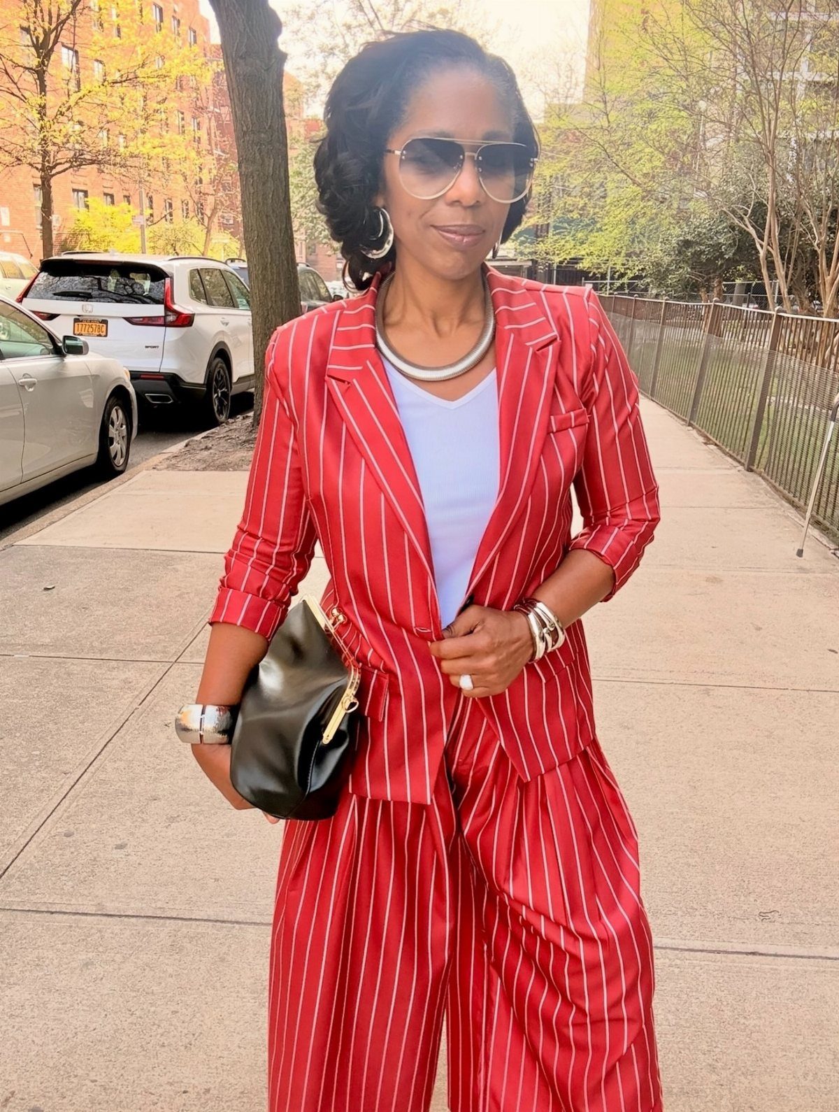 A woman in a red pinstriped suit and sunglasses standing on a city sidewalk.