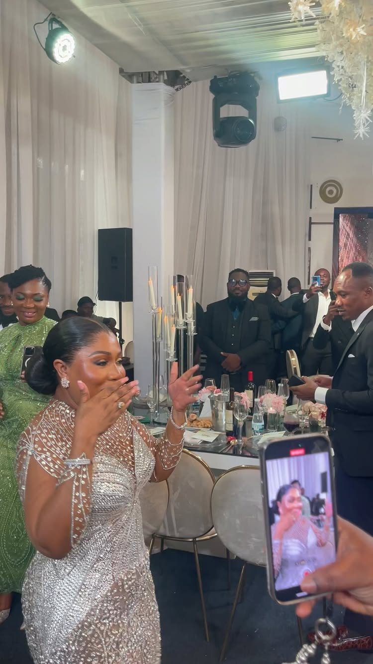 A woman in a silver sequined gown reacts with joy at a formal banquet dinner.