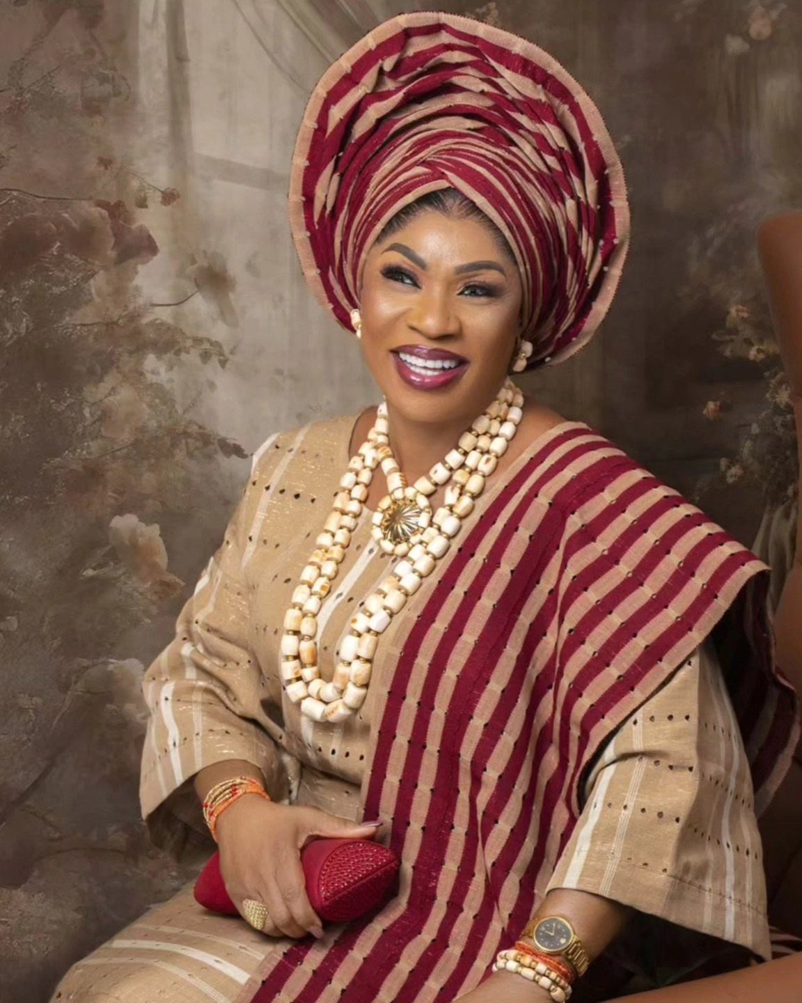 Smiling woman in traditional Nigerian attire with a large headwrap and beaded necklaces.