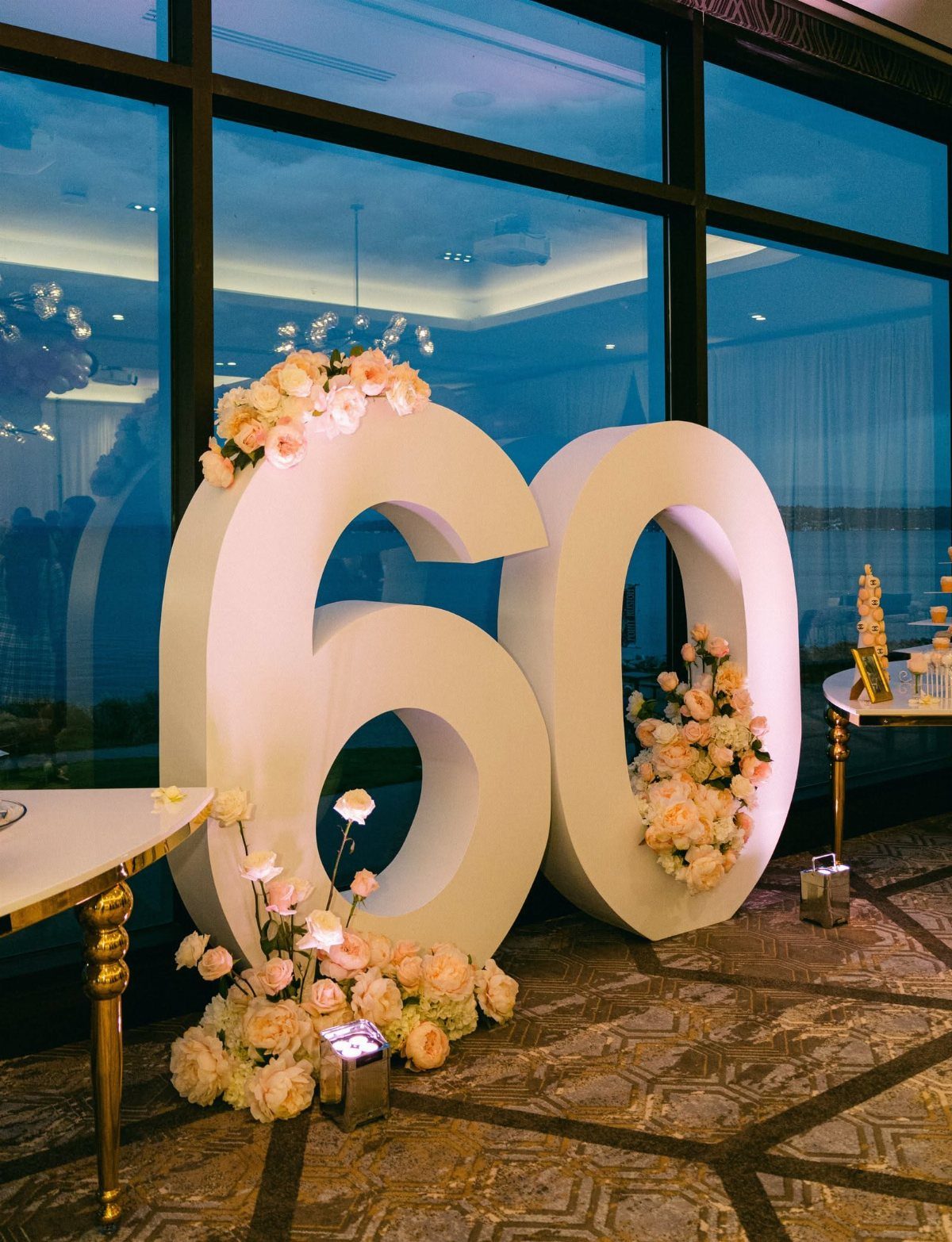 Large white 3D numbers sixty decorated with peach and white flowers in a room.
