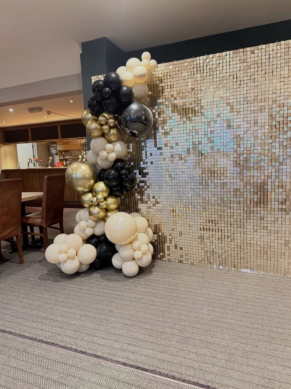 A balloon garland in black, gold, and cream colors against a gold sequin backdrop.