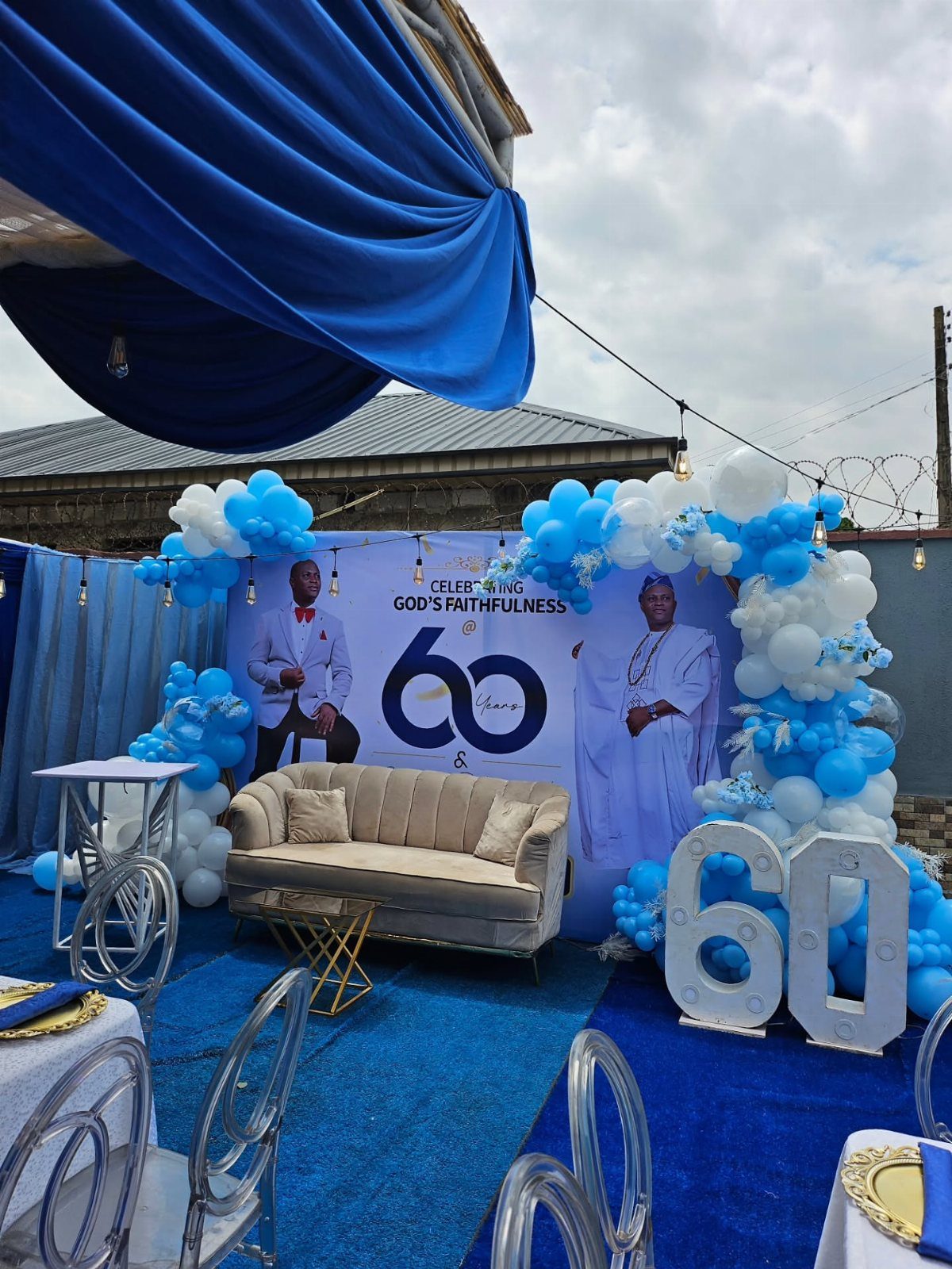 Blue and white balloon arch surrounding a 60th birthday celebration backdrop and sofa.