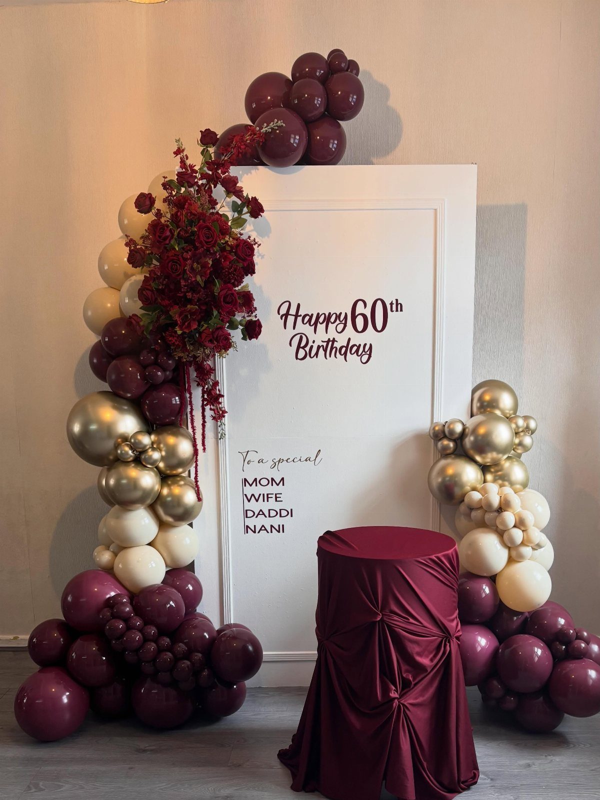 Maroon, gold, and cream balloons decorating a white backdrop with Happy 60th Birthday text.