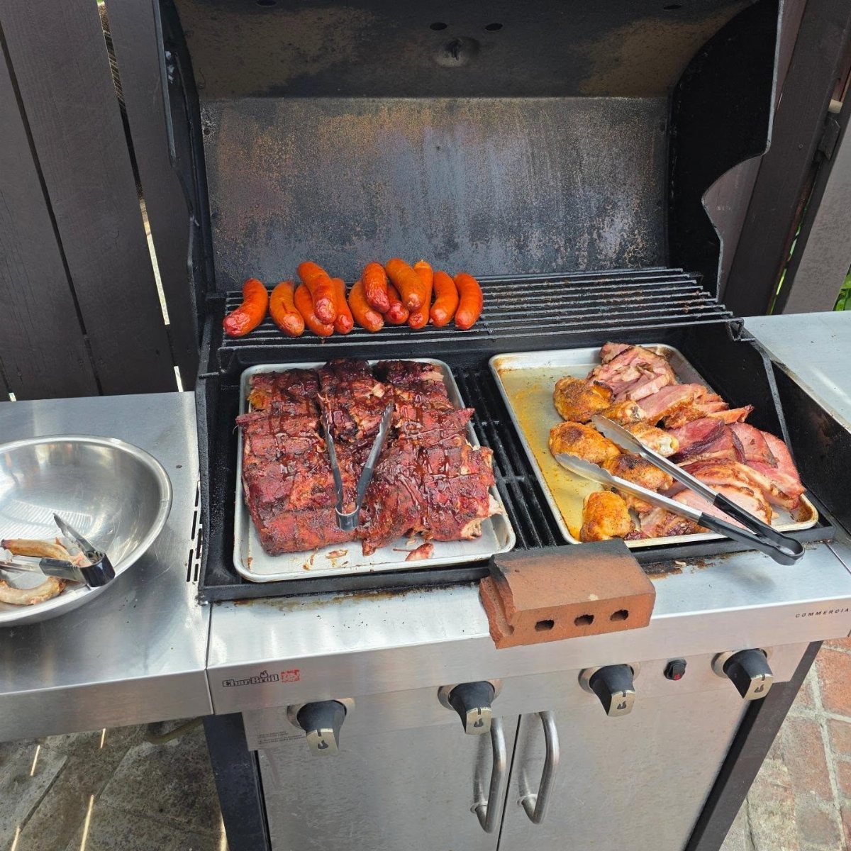 Sausages, ribs, and chicken cooking on a large stainless steel outdoor gas grill.