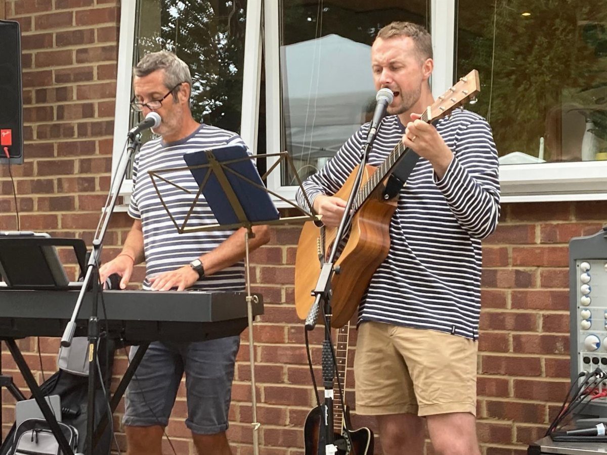 Two men performing acoustic music with a guitar and keyboard in an outdoor setting.