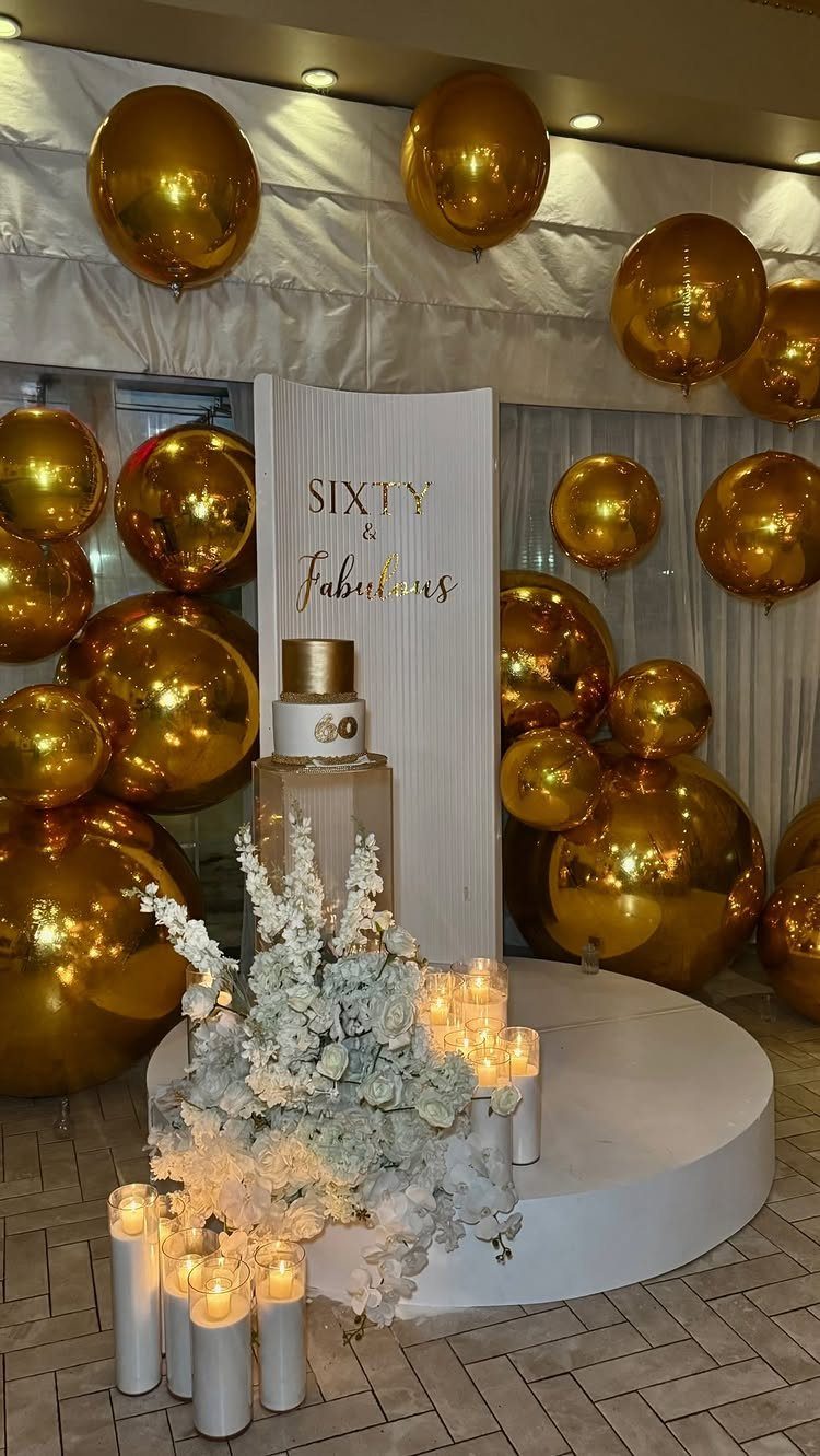Gold balloons and white flowers surround a sign that says Sixty and Fabulous.