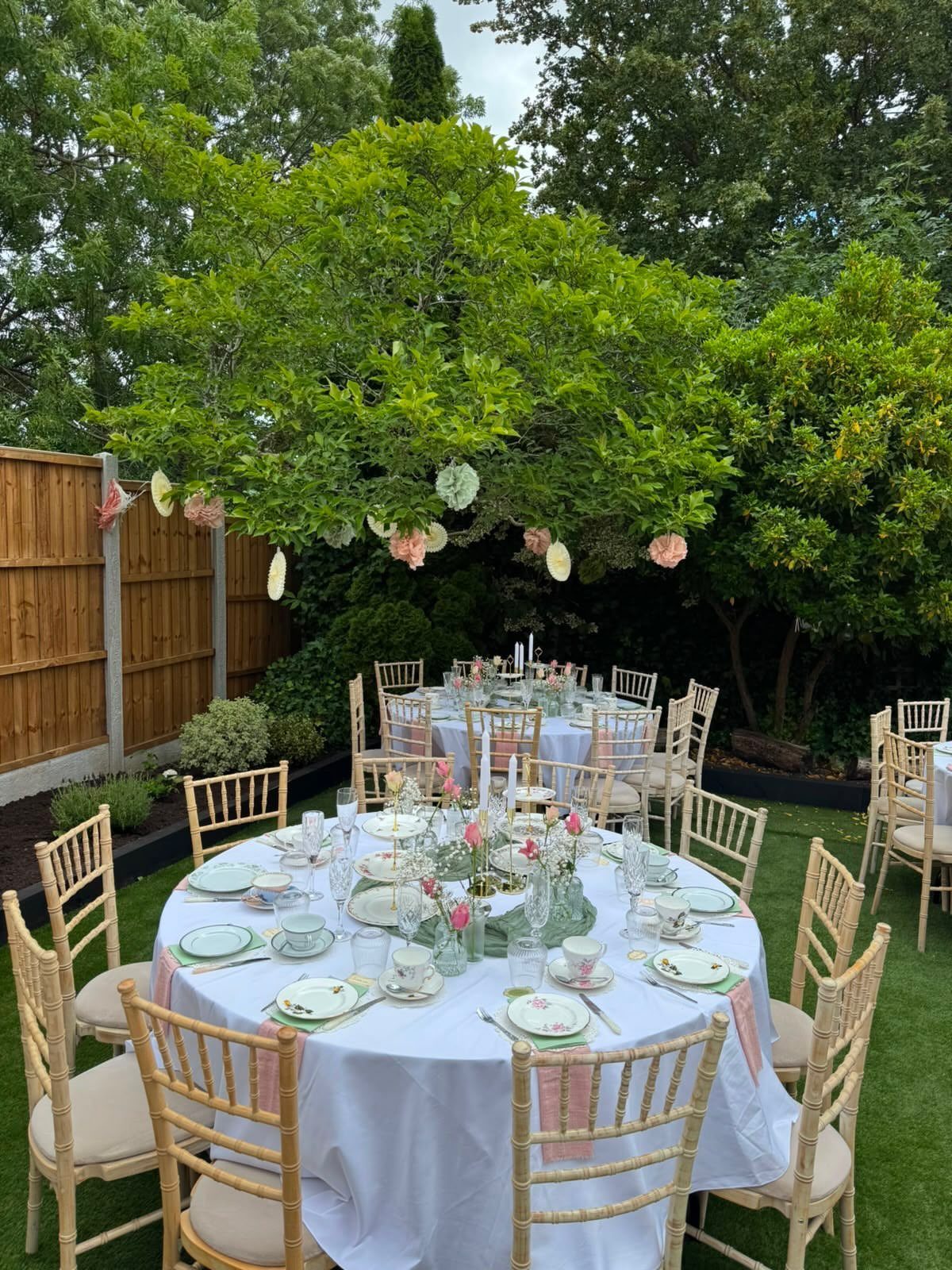Elegant garden tea party setup with floral centerpieces and teacups on round tables.