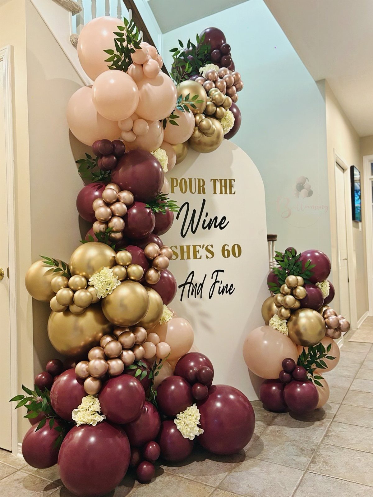 Balloon garlands in burgundy and gold surrounding a white sign celebrating a 60th birthday.