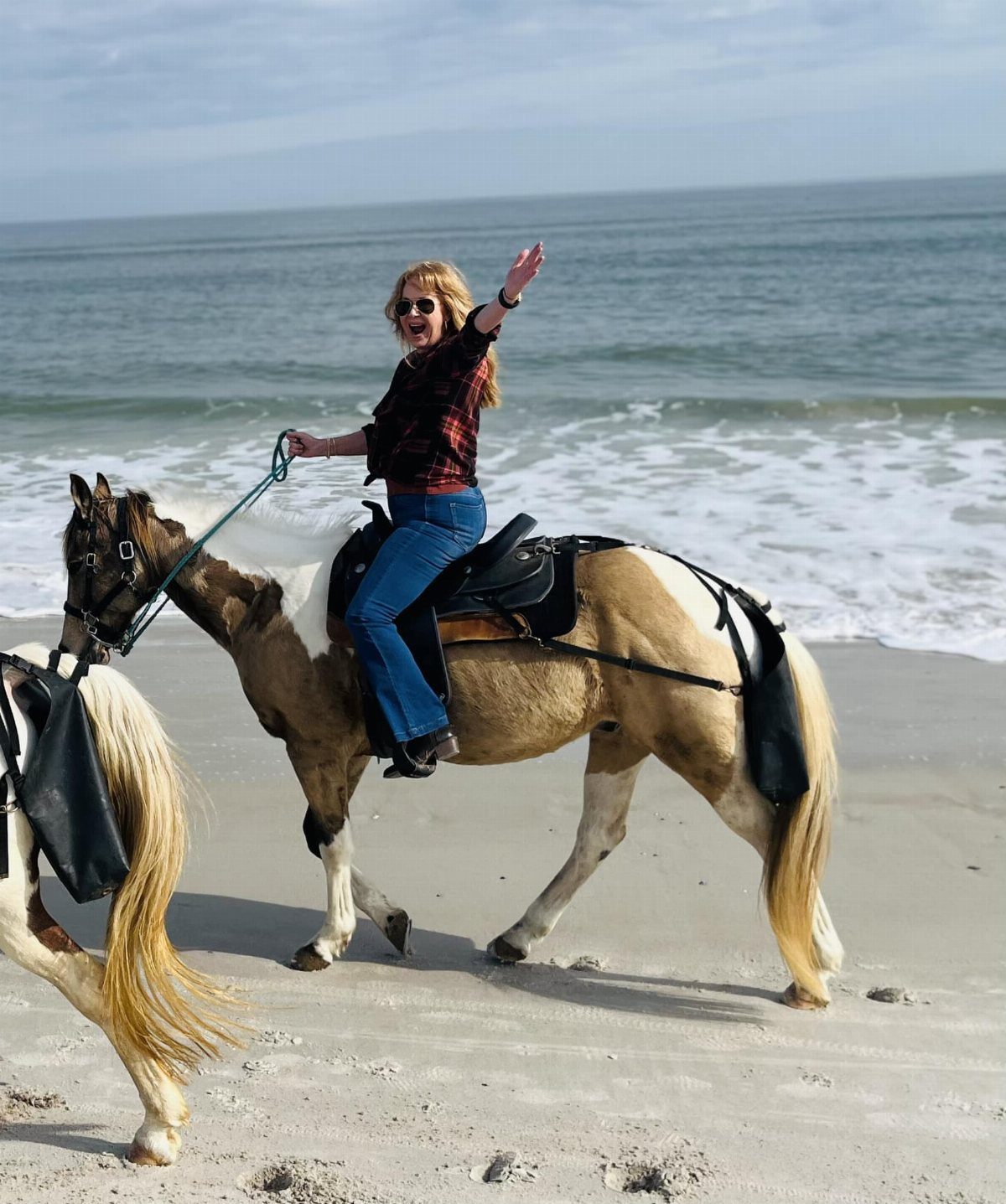 A woman riding a patterned horse on a sandy beach while waving her hand.
