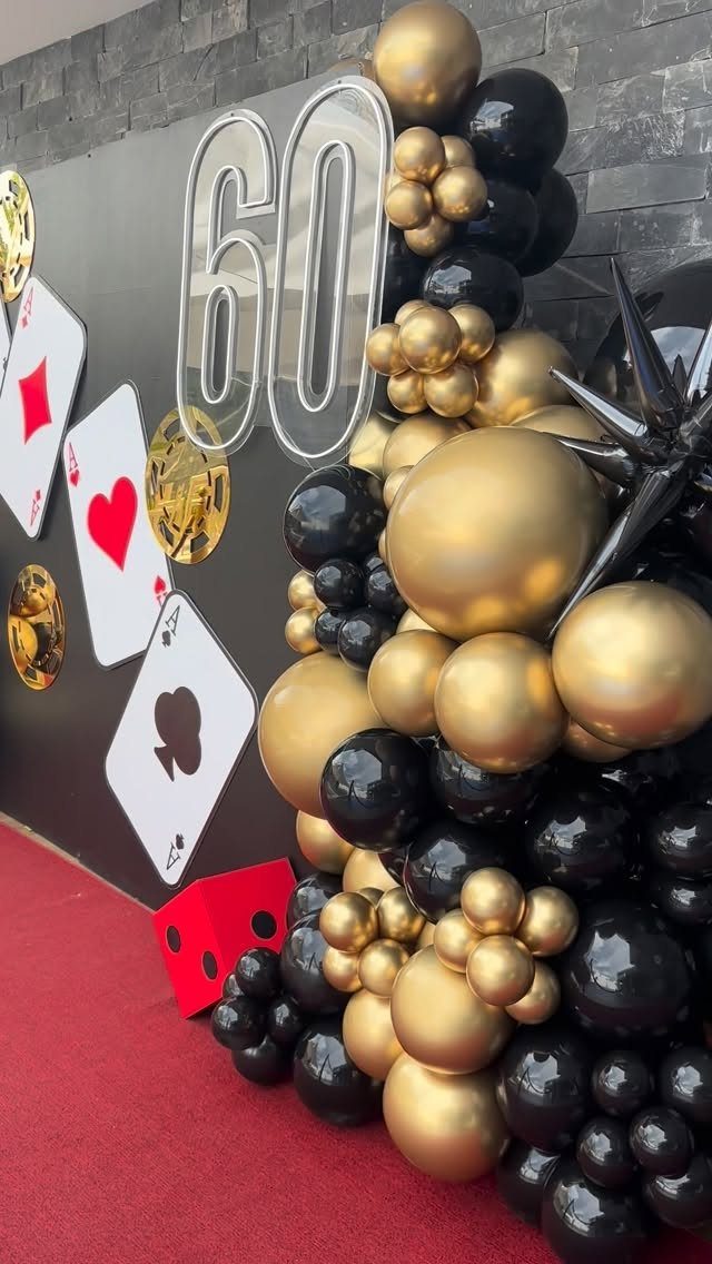 Large silver number sixty against a black backdrop with gold and black balloons and playing cards.