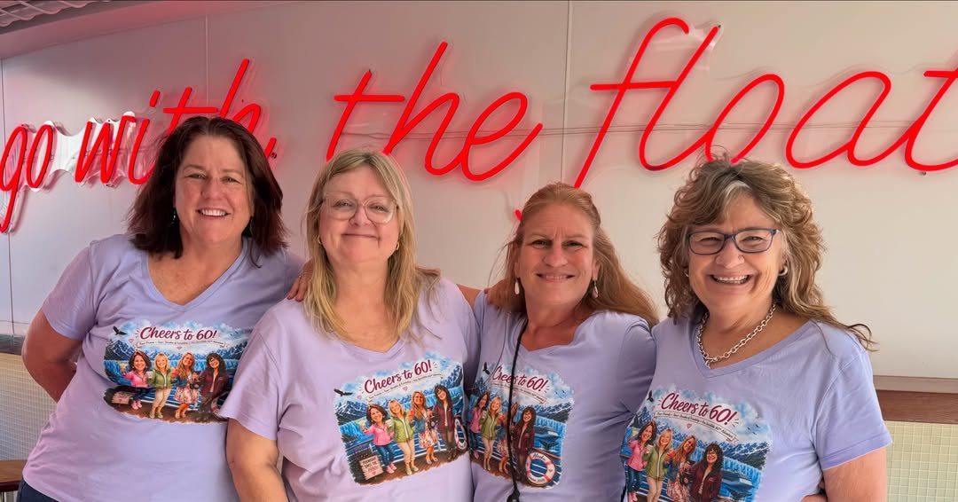 Four smiling women wearing matching purple t-shirts celebrating a 60th birthday milestone.