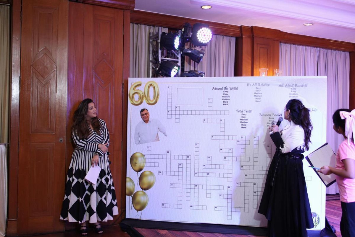 Two women standing beside a large custom crossword puzzle board for a 60th birthday celebration.