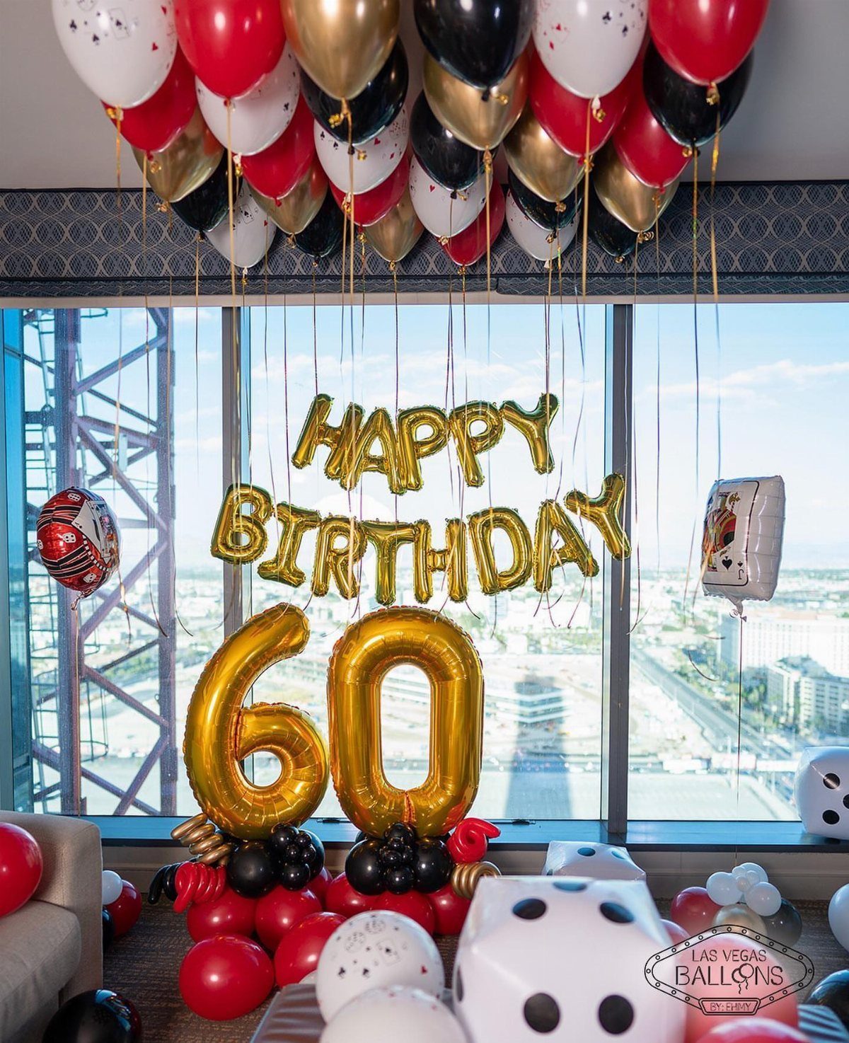 Gold, red, and black balloons decorate a room with a large window overlooking a city skyline.
