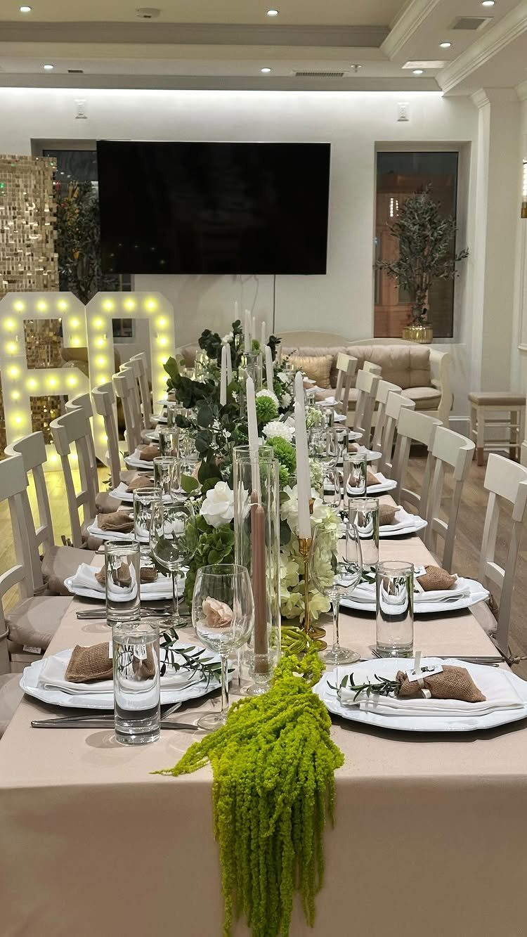 An elegantly set long dining table with greenery and large illuminated numbers sixty in the background.