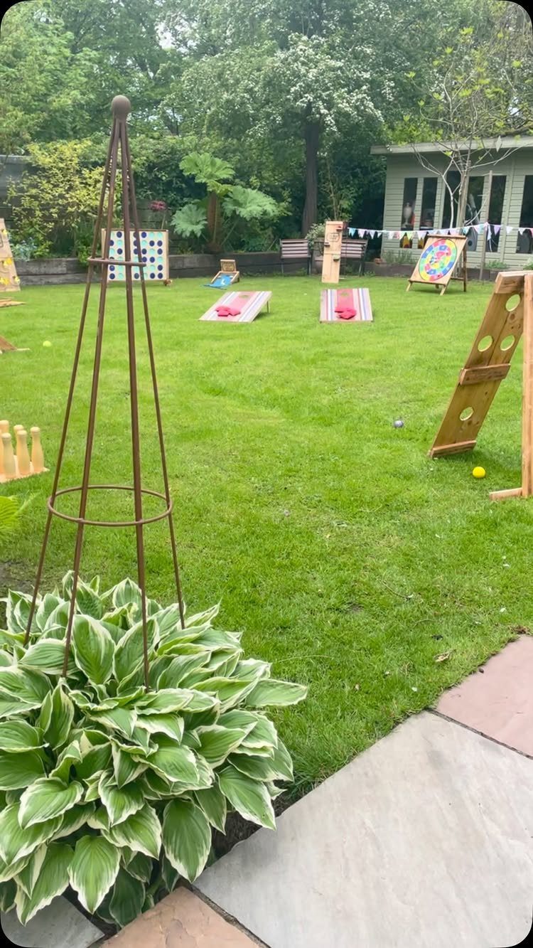 Wooden lawn games and cornhole boards set up on a lush green backyard lawn.
