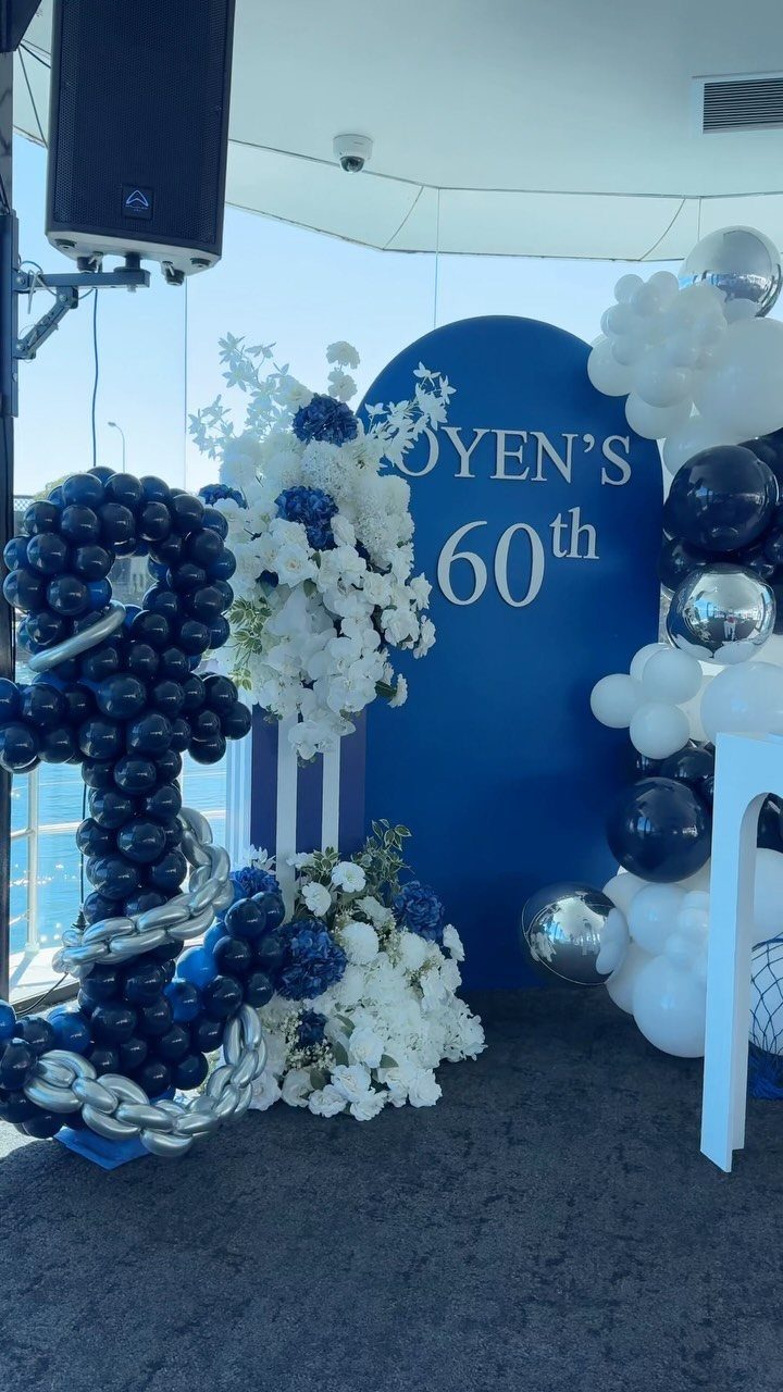 Blue and white balloon decorations with floral arrangements and a large navy blue balloon anchor for a 60th birthday.