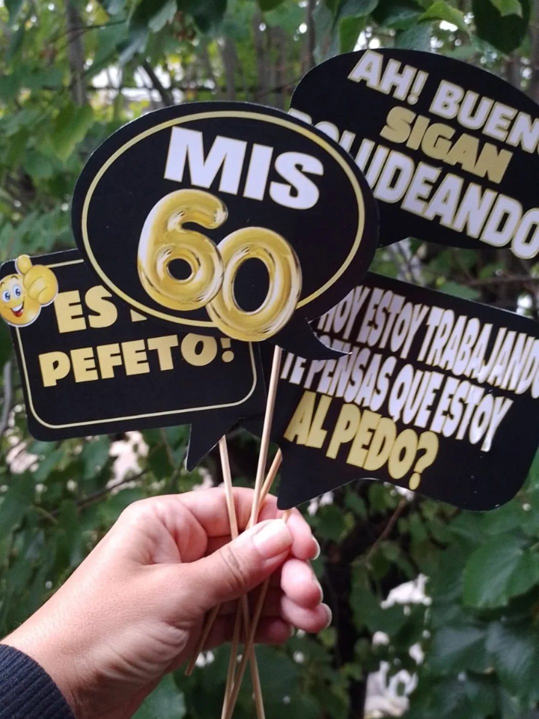 Hand holding several black speech bubble party props with Spanish text and gold numbers.