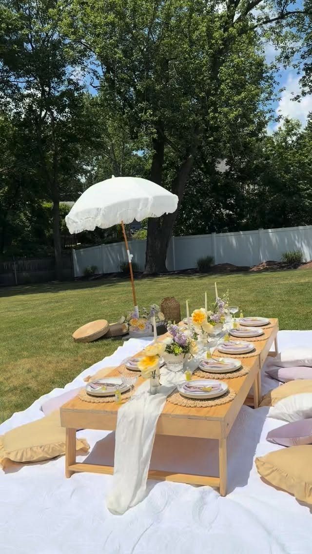 A low wooden picnic table set with flowers and plates on a white cloth outdoors.