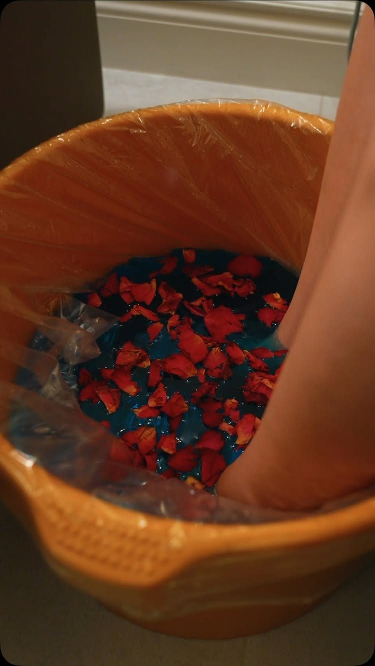 A foot soaking in blue water with red flower petals inside an orange basin.