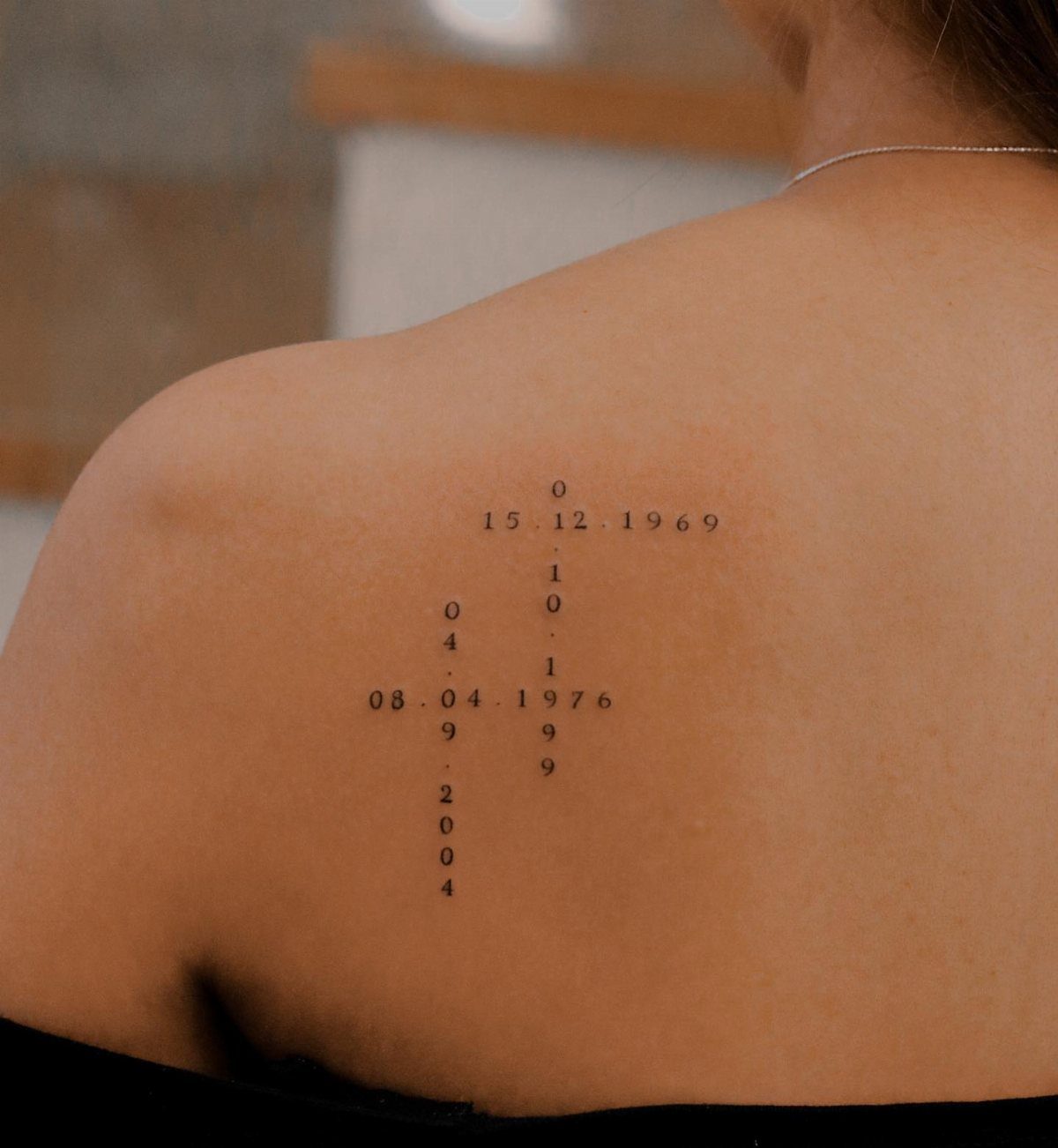 Minimalist black ink number tattoos arranged in a geometric pattern on a person's shoulder.