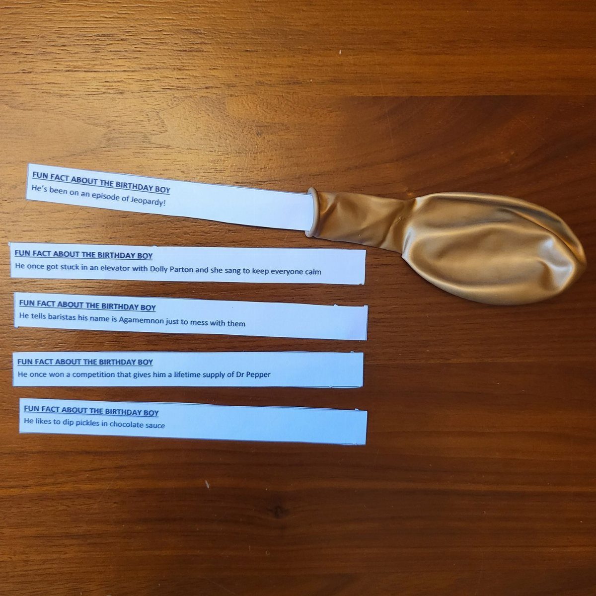 Gold balloon and printed fun fact strips on a wooden table.