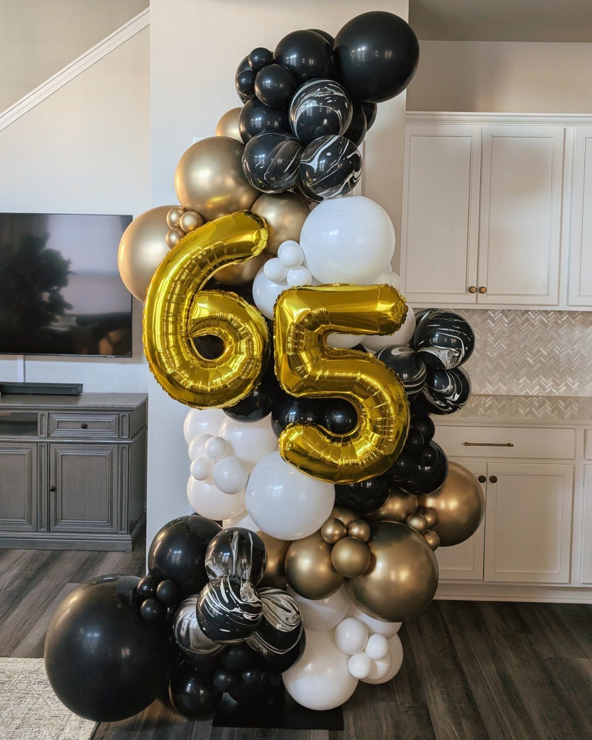 Large balloon garland with black, white, and gold balloons and gold number 65 balloons.